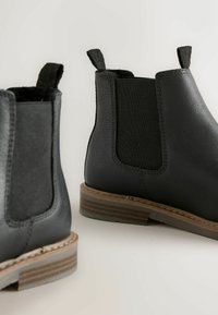 Czarne botki za kostkę wykonane ze skóry, z elastycznymi panelami po bokach, teksturowaną powierzchnią oraz podeszwą warstwową z brązowym akcentem.