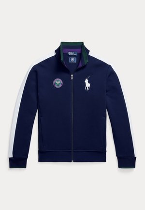 Veste zippée bleu marine avec panneaux latéraux blancs, accents verts et un logo Wimbledon. Dotée d'un col montant et d'une texture de tissu lisse.