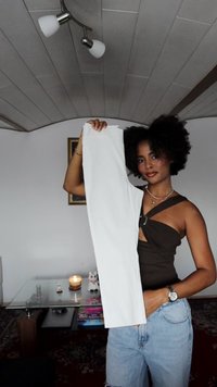 Pantalones blancos exhibidos, tela suave, diseño de cintura alta, combinados con una blusa marrón. El fondo incluye una mesa de cristal y elementos decorativos.