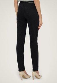 Svarta åtsittande jeans med en slät textur, medelhög midja och två bakfickor, i kombination med beige högklackade skor.