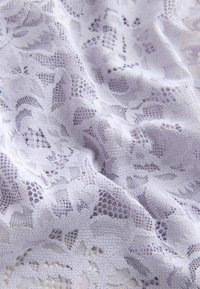 Tissu en dentelle blanche avec motifs floraux et géométriques, présenté en plis doux et en gros plan.