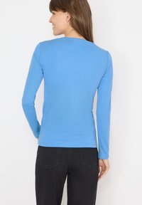 Lange mouw shirt in lichtblauwe katoen, met een ronde hals en een slim fit ontwerp. Gemaakt met donkere zwarte broeken, minimale zichtbare details.