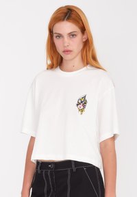 Camiseta corta blanca hecha de algodón suave. Presenta un diseño gráfico colorido en el lado izquierdo del pecho. Manga corta y corte relajado.