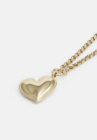 Collana d'oro con pendente a forma di cuore lucido inciso con la scritta "Calvin Klein" su sfondo bianco.