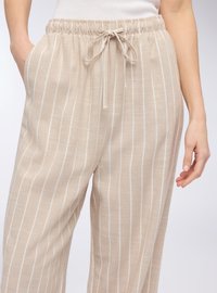 Pantaloni beige in misto lino con righe verticali bianche. Vita elastica con cordino e tasche laterali. Vestibilità loose e texture leggera.