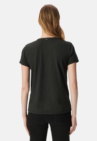 Camiseta negra de manga corta con cuello redondo, textura suave y un pequeño logo en el cuello, combinada con pantalones negros.
