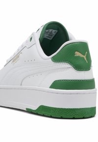 Hvide lædersneakers med grønne accenter, guld Puma-logo, tekstureret hælkap og kontrastfarvet gummisål. Klassisk lav profil.