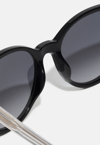 Lunettes de soleil en plastique noir avec de grandes lentilles rondes présentant un léger dégradé. Branches en argent texturé et fin. Fini brillant.