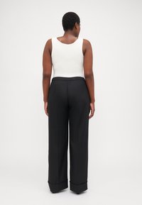 White sleeveless top paired with black wide-leg trousers featuring an elastic waistband and folded cuffs, shown from the back.