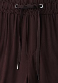 Close-up of dark brown pants with elastic waistband and tied drawstring featuring metal aglets and eyelets.