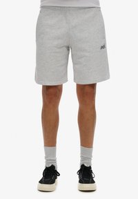 Pantalones cortos de algodón grises con una cintura elástica, bolsillos laterales y un logo impreso. Se llevan con calcetines grises y zapatillas negras.