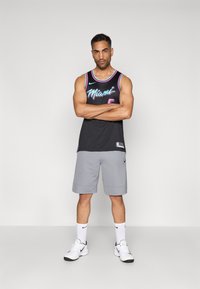 Svart baskettröja med "Miami" grafik i rosa och blått, tillsammans med grå shorts. Vita sneakers och strumpor kompletterar den atletiska looken.