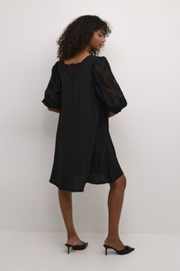 Vestido negro con mangas abullonadas de encaje, escote en v en la espalda y ajuste holgado, hecho de una tela ligera, combinado con tacones negros de punta.