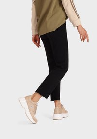 Sneaker in suede beige con suole in gomma bianche, dotate di lacci e dettagli ricamati. Indossate con jeans neri a vita alta.