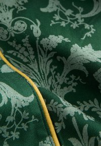 Tessuto verde con un motivo floreale in grigio chiaro. Include una finitura gialla lungo la cucitura. Tessitura liscia con dettagli intrecciati.