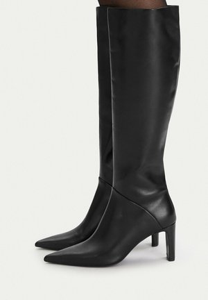 Czarne kozaki skórzane za kolano, z ostrymi noskami i obcasami średniej wysokości, na jednolitym białym tle.