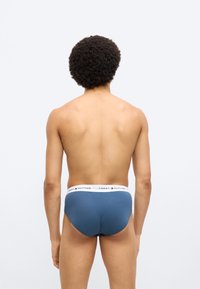 Μπλε βαμβακερό σλιπ με λευκή μέση που φέρει το λογότυπο "TOMMY HILFIGER", με λεία υφή και εφαρμοστή σχεδίαση. Εμφανίζεται η πίσω όψη.