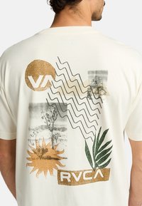 Cream cotton t-shirt featuring abstract prints in gold, green, and black, including sun, waves, and tree motifs with RVCA logo.