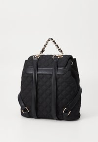 Black quilted backpack made of fabric with leather accents. Features chain handle, adjustable shoulder straps, and a textured surface.