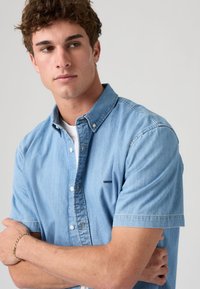 Jasnoniebieska koszula jeansowa z krótkim rękawem i kołnierzykiem na guziki, z małym logo Levi's i luźnym krojem. Gładka tekstura i klasyczny design.