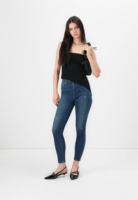Svart axelbandslös topp, blå slim-fit jeans och svarta klackar med ankelrem. Slät tyg, figursydd design och subtila slitningar på jeansen.