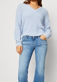 Ljusblått stickat tröja med v-ringning, vågig halsringning och ribbad textur, kombinerad med ljusa denim flare jeans.