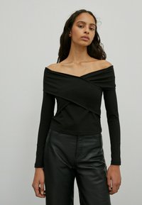 Schwarzes, trägerloses Langarmoberteil mit gewickeltem Design, aus weichem Stoff gefertigt. Hat eine schmale Passform und kontrastierende Nähte, kombiniert mit schwarzen Hosen.