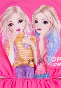 Grafisches Oberteil mit zwei Cartoon-Mädchen mit langen, hellen Haaren. Eines trägt ein gelbes gestreiftes Shirt, das andere ein einfarbiges pinkes Oberteil. Heller pinker Hintergrund.