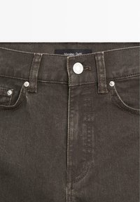 Pantalon en denim marron foncé avec fermeture par bouton argenté, passants de ceinture et poches avant, avec une étiquette Massimo Dutti visible à l'intérieur de la ceinture.