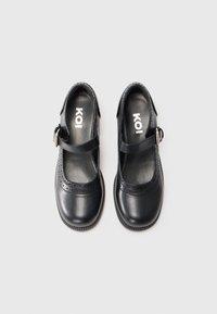 Black leather Mary Jane shoes with a rounded toe, perforated detail on the strap, and a flat rubber sole. Adjustable buckle closure.
