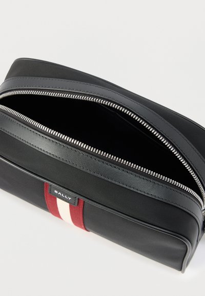 Μαύρο ορθογώνιο τσαντάκι με κόκκινη και λευκή λωρίδα, ασημί φερμουάρ μερικώς ανοιχτό και ετικέτα με την επωνυμία Bally μπροστά.