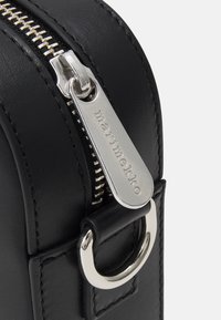 Borsa in pelle nera con zip in argento. Presenta un'etichetta con logo e una maniglia ad anello. Texture liscia con linee pulite e design minimal.