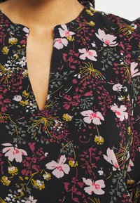 Tissu noir avec un motif floral comprenant des fleurs roses, jaunes et vertes. Encolure en V avec une coupe modeste et une texture douce.