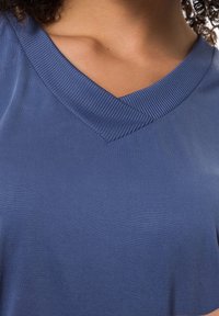 Top en V bleu marine en tissu avec un col côtelé texturé. Le matériau est lisse, offrant une coupe décontractée et un design simple.