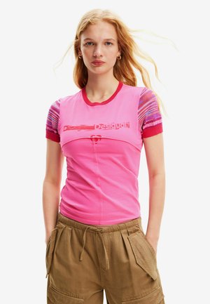 Camiseta rosa de manga corta con un patrón texturizado en las mangas, cuello acanalado y diseño impreso en la parte delantera, combinada con pantalones cargo beige.