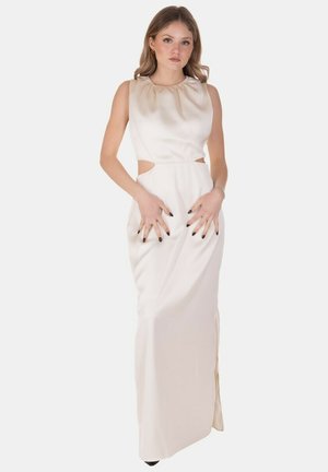 Donna che indossa un abito di raso bianco senza maniche con ritagli laterali, in piedi davanti a uno sfondo bianco uniforme.