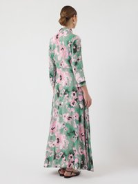 Robe longue fleurie en tissu vert avec des motifs roses et noirs. Elle présente un col et des manches trois-quarts. Ourlet aplati.