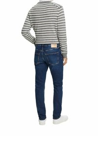 Pull rayé gris et blanc à col rond, associé à un jean bleu foncé avec poches arrière et une étiquette en cuir de marque. Baskets blanches.