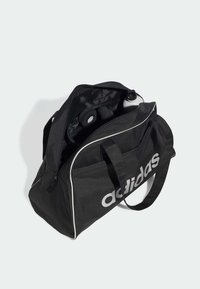Mustan värinen duffelipussi vetoketjulla, jossa on valkoiset viivat ja adidas-logo. Sisällä näkyy vesipullo ja muita varusteita.