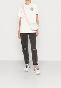 Světle béžové tričko s grafikou slunce, šedé roztrhané džíny a bílé tenisky s černými akcenty. Malá světle modrá a růžová crossbody taška.