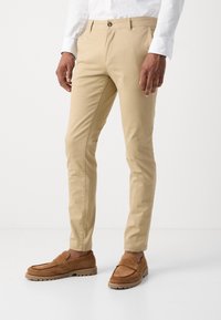 Beige chinos met een slim fit, een platte voorkant en een knoopsluiting, gecombineerd met bruine suède instappers met een gestructureerd ontwerp en een rubberen zool.