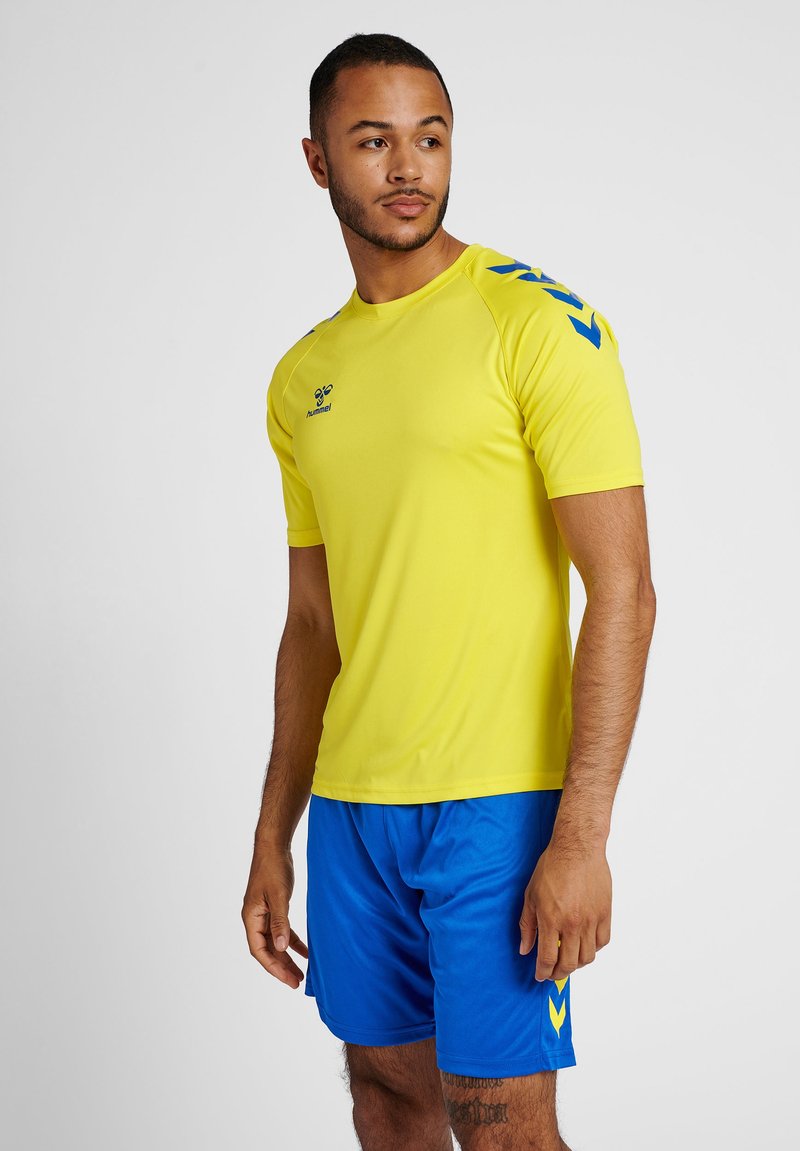 Camiseta deportiva de un brillante color amarillo con acentos azules en los hombros, combinada con pantalones cortos azules. Fabricada con un tejido ligero y que absorbe la humedad.