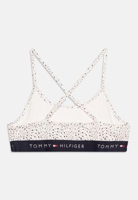 Bralette blanca con un patrón geométrico, tirantes cruzados en la espalda, cintura ancha en color azul marino con el logo "TOMMY HILFIGER" en blanco.