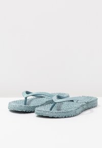 Ljust blå flip-flop-sandaler med en texturerad sula. Remmarna har en blank, glittrig yta. Designen är enkel med en klassisk tanga-stil.