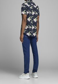 Maglietta a maniche corte, blu navy con fiori, presenta fiori bianchi e rosa con foglie verdi, abbinata a jeans blu e sneakers bianche.