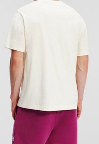 Short-sleeve t-shirt in off-white cotton, relaxed fit, plain design, visible stitching, paired with purple sweatpants featuring logo.