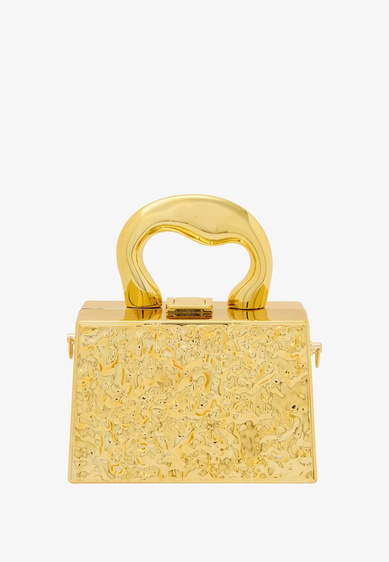 Guldväska med en texturerad yta, trapezformad design och ett slätt, böjt handtag. Har en metallspänne och en glänsande yta.