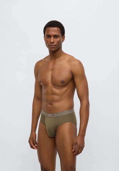 Męskie majtki w kolorze oliwkowej zieleni z wzorzystym elastycznym pasem. Materiał wydaje się gładki, dopasowany o niskim stanie.