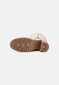 Bota color crema con suela de goma texturizada, que presenta un patrón de banda de rodadura en zigzag y cremallera lateral, mejorando la tracción y el soporte.