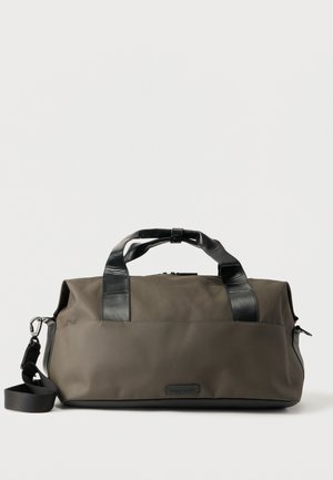 Ciemnooliwkowa torba podróżna z czarnymi skórzanymi uchwytami i odpinanym paskiem na ramię na białym tle.